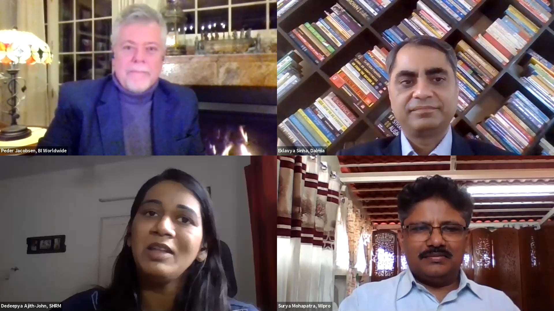 Four people are in a video call. Top left: Person with gray hair and beard in front of a fireplace. Top right: Person with bookshelves. Bottom left: Person with long hair. Bottom right: Person with mustache and glasses in a room with a patterned wall.