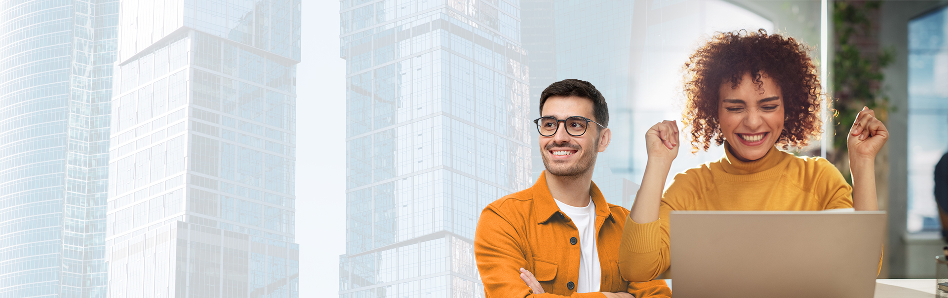 A man and woman sit together, smiling and looking at a laptop screen. Both wear bright clothing. The background shows tall glass buildings, blending with the indoor scene.