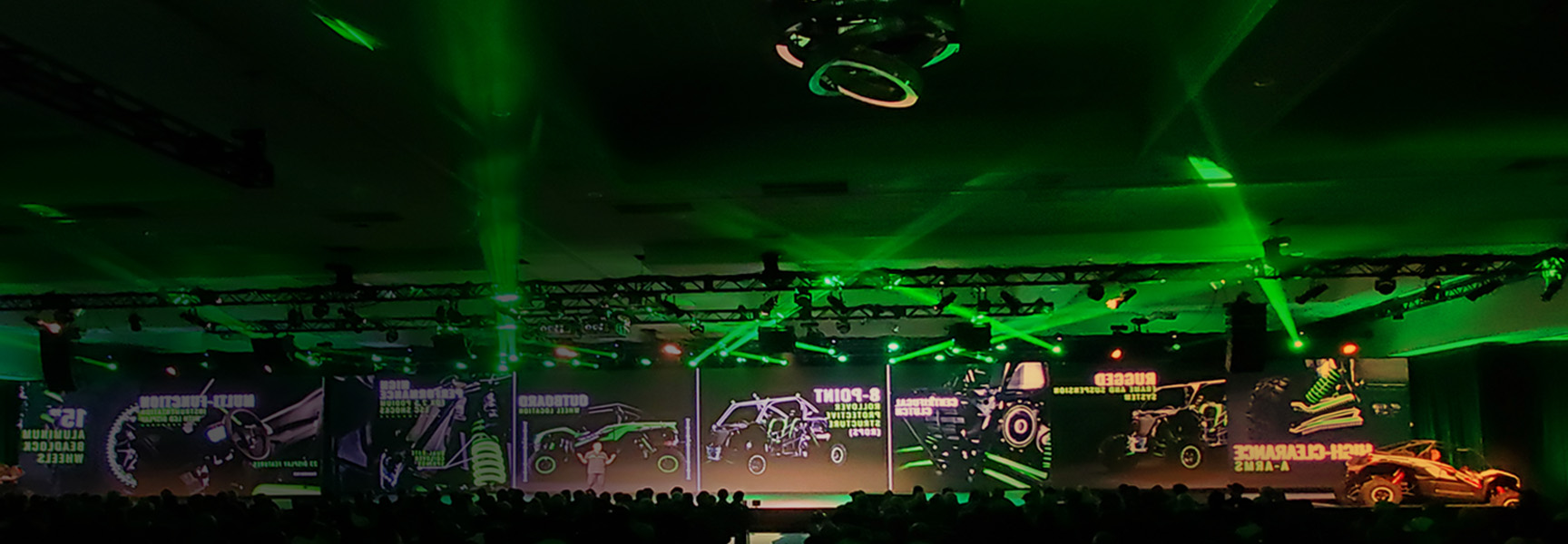 A stage with vibrant green lighting and projections displaying various tractors and agricultural machinery. A seated audience watches the presentation, creating a dynamic and futuristic atmosphere.