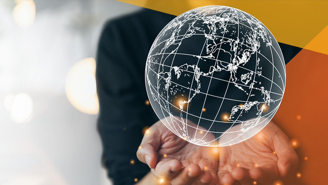 Hands are shown holding a digitally-rendered glowing globe with white grid lines, representing continents. The background is softly blurred with warm lights and abstract orange and gray shapes.