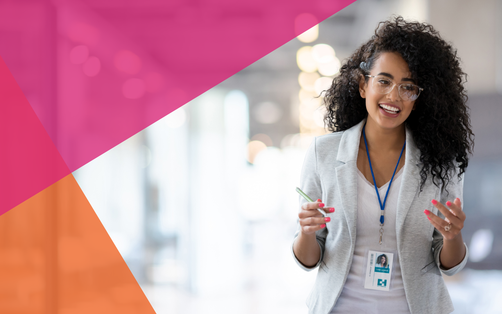 A smiling woman with curly hair, glasses, and a badge, stands indoors holding a pen. She wears a light blazer and white top. Pink and orange geometric shapes overlay the top left corner of the image.
